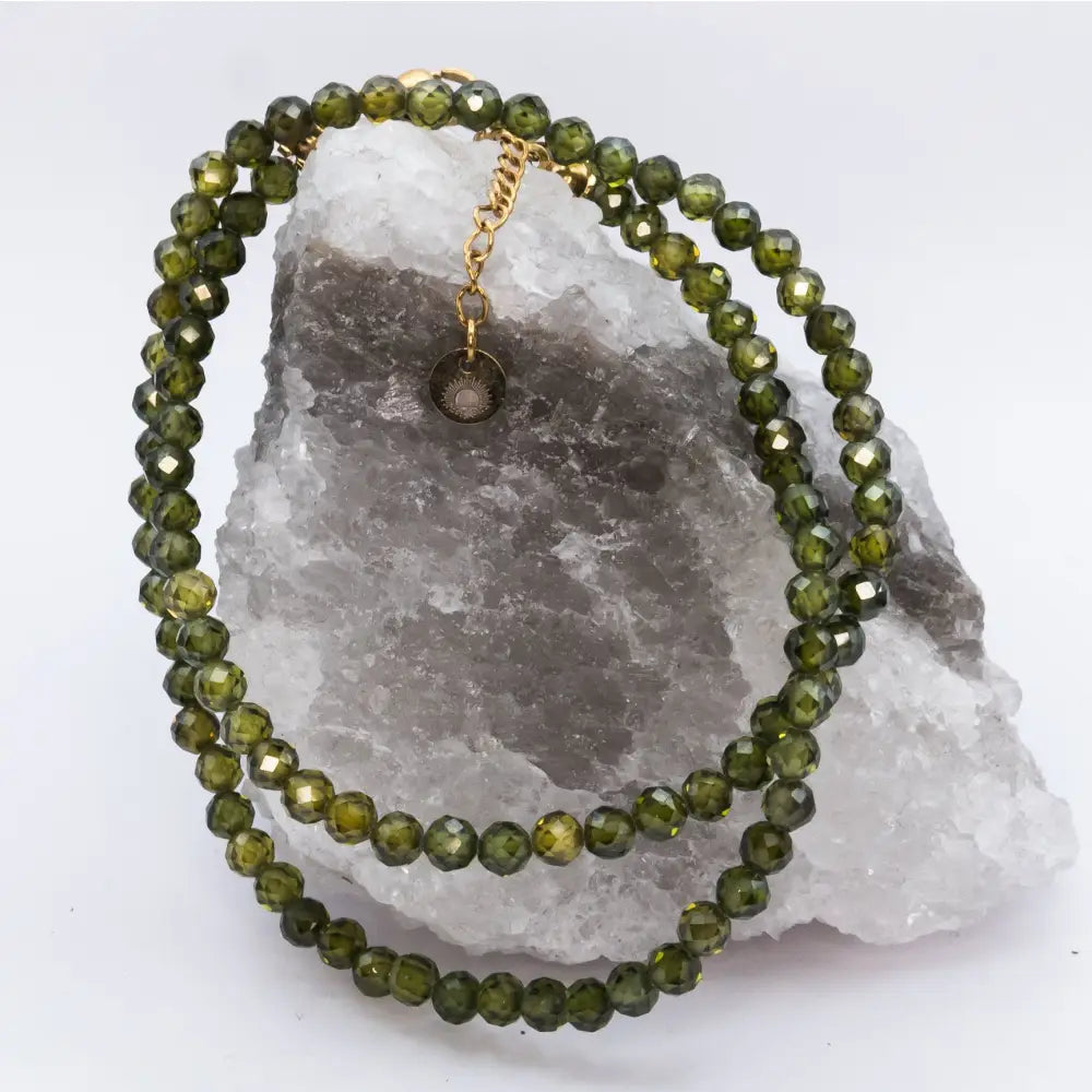Peridot Faceted Necklace with gold charm on a white and grey stone and neutral background