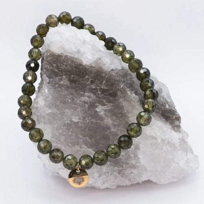 Peridot Faceted Bracelet with gold charm on a white and grey stone with light background