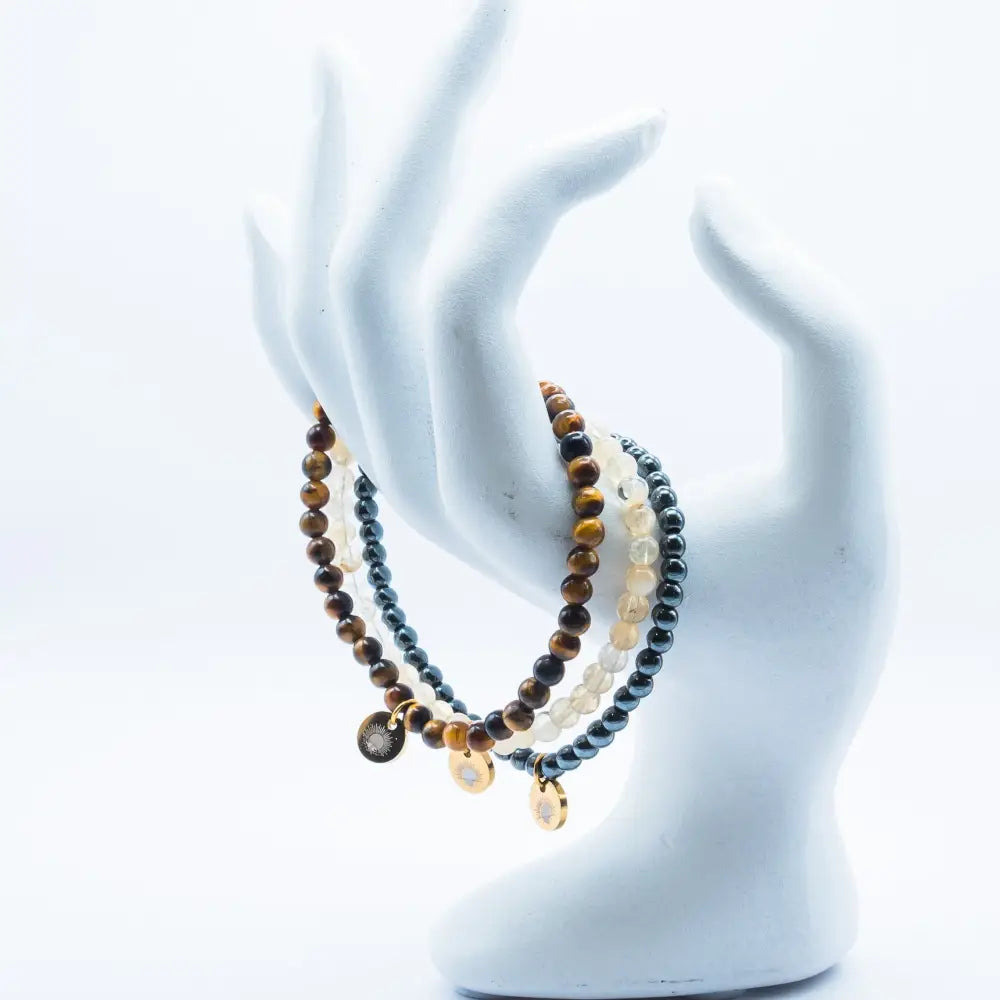 Set of Tiger Eye, Hematite, and Citrine beaded bracelets with gold charms on a white mannequin hand against a white background