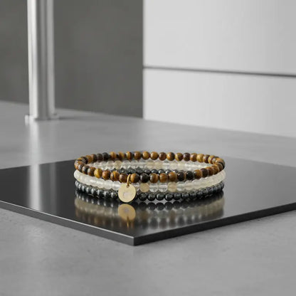 Set of Tiger Eye, Hematite, and Citrine beaded bracelets with gold charm on a black square platform with a neutral background
