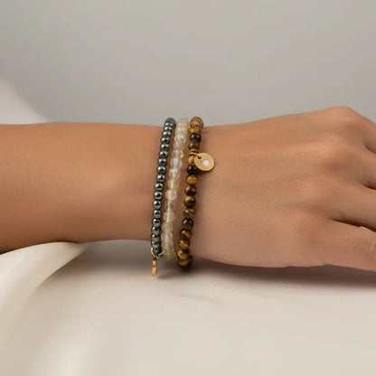 Hand wearing Tiger Eye, Hematite, and Citrine beaded bracelets with gold charms on a neutral background