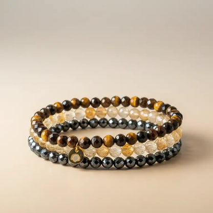 Set of Tiger Eye, Hematite, and Citrine faceted beaded bracelets with gold charm on a beige background