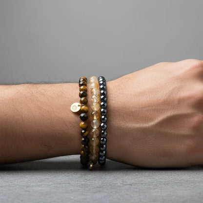 Hand wearing Tiger Eye, Hematite, and Citrine faceted beaded bracelets with gold charm on a gray background