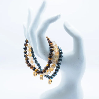 Set of Tiger Eye, Hematite, and Citrine faceted beaded bracelets with gold charms on a white mannequin hand against a white background