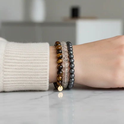 Person wearing Tiger Eye, Hematite, and Citrine faceted beaded bracelets with gold charm on a neutral background