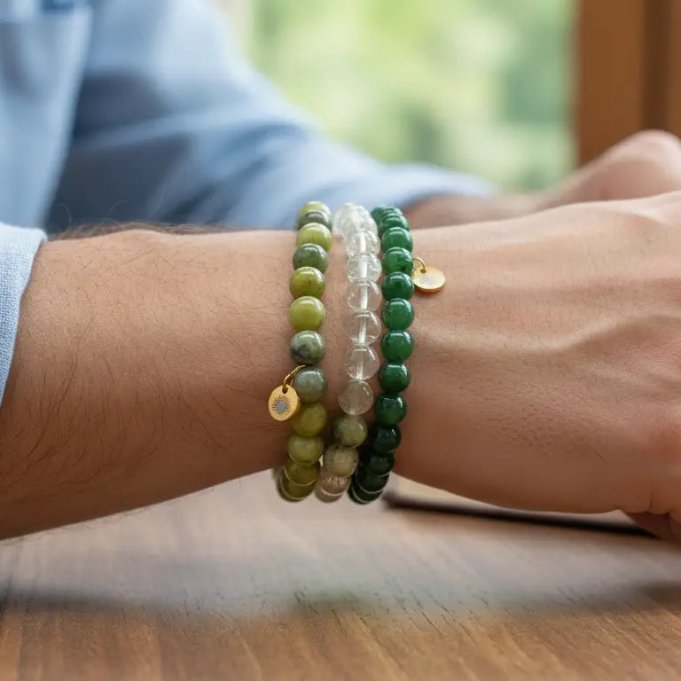 Person wearing Peridot, Nephrite Jade, and Citrine beaded bracelets with gold charms on a wooden surface and blurred background