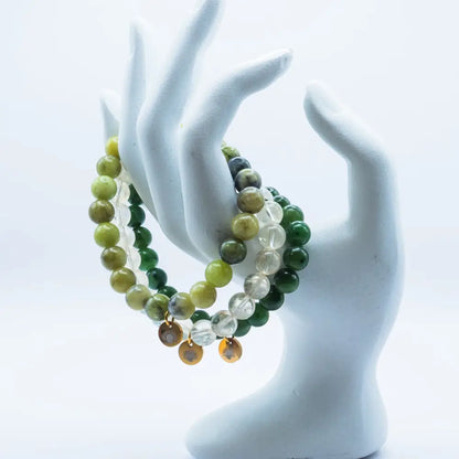 Set of Peridot, Nephrite Jade, and Citrine beaded bracelets with gold charms on a white mannequin hand against a white background