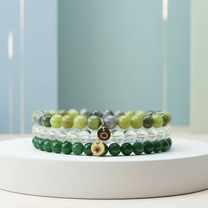 Stack of Peridot, Nephrite Jade, and Citrine beaded bracelets with gold charms on a white platform with a light blue background
