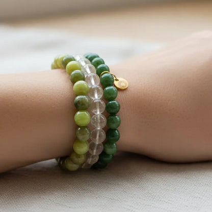 Close-up of a wrist wearing Peridot, Nephrite Jade, and Citrine beaded bracelets with gold charm on a neutral background
