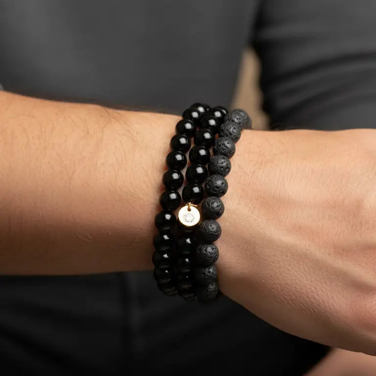 Person wearing Black Tourmaline, Obsidian, and Lava Stone beaded bracelets with gold charm on a neutral background