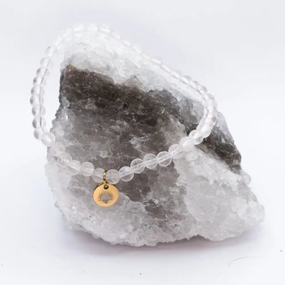 Rose Quartz Beaded Bracelet with gold charm on a white and grey stone and a neutral background