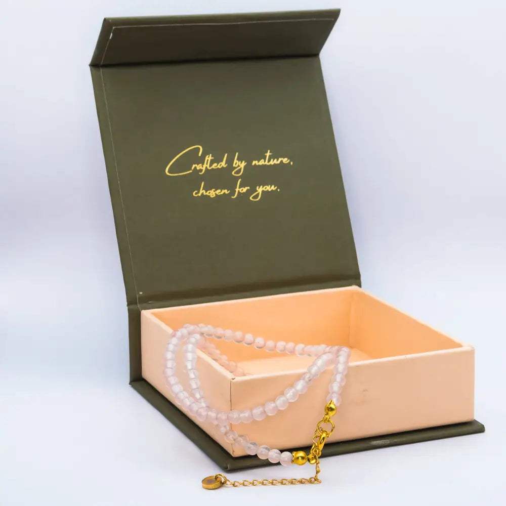Rose Quartz Beaded Necklace with gold charm on a cream and olive green branded box and light grey background