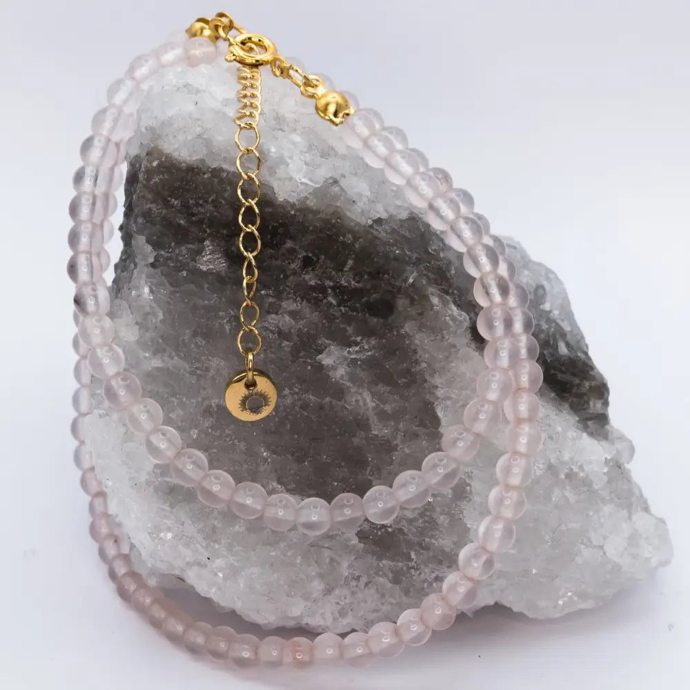 Rose Quartz Beaded Necklace with a gold charm on a white and grey stone and neutral background