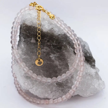 Rose Quartz Beaded Necklace with a gold charm on a white and grey stone and neutral background