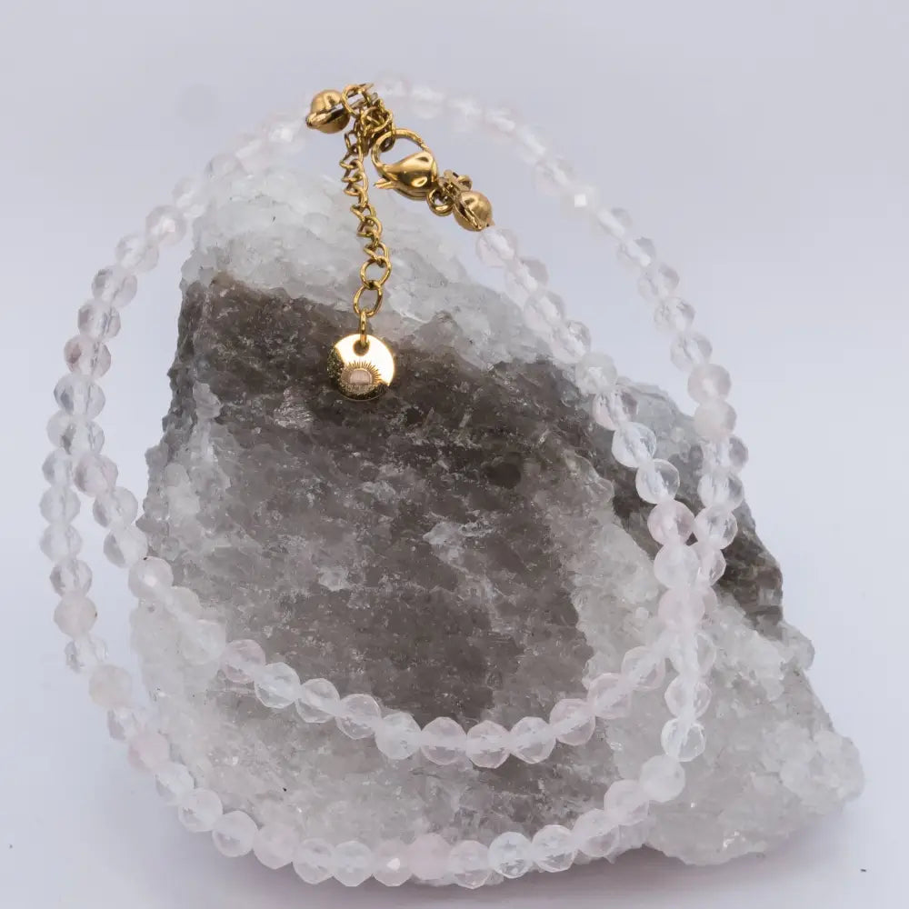 Rose Quartz Faceted Necklace with a gold charm on a white and grey stone and light grey background
