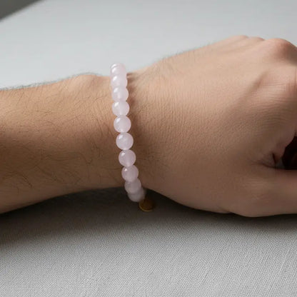 Rose Quartz Beaded Bracelet with gold charm on a wrist against a light fabric