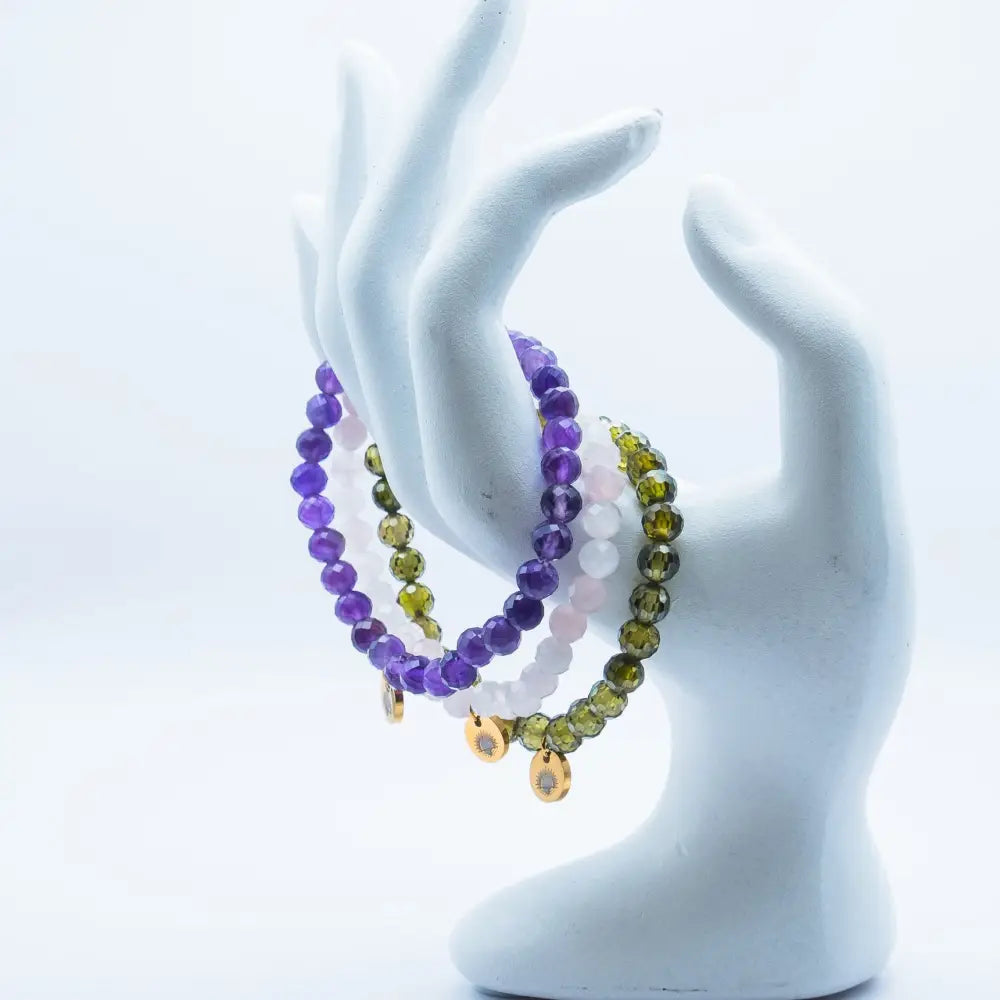 Set of Rose Quartz, Amethyst, and Peridot faceted beaded bracelets with gold charms on a white mannequin hand against a white background