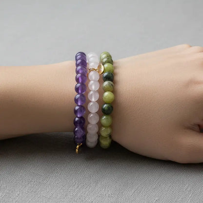 Hand wearing Rose Quartz, Amethyst, and Peridot beaded bracelets with gold charms on a gray background