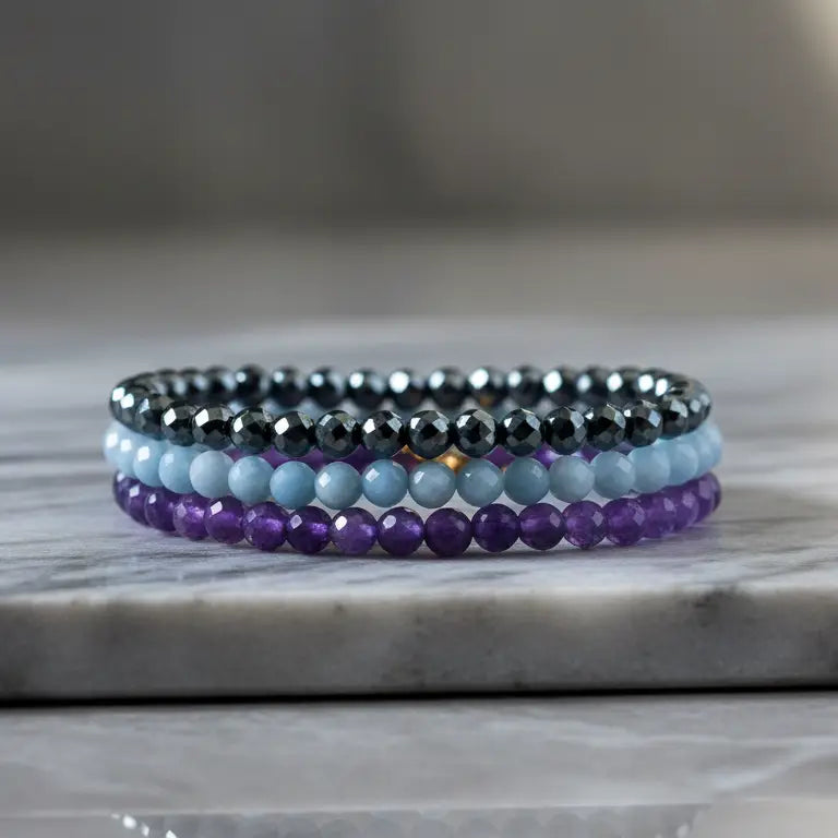 A set of Amethyst, Angelite, and Hematite faceted bracelets on a marble stand and blurred background