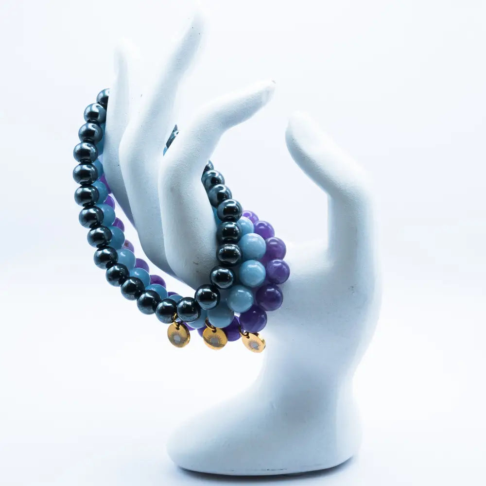 Amethyst, Angelite, and Hematite beaded bracelets with gold charms on a mannequin hand with white background