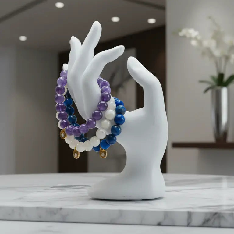 Decorative display of Amethyst, Moonstone, and Lapis Lazuli beaded bracelets with gold charm on a white hand sculpture with a blurred indoor background.