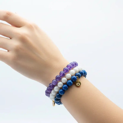 Hand wearing Amethyst, Moonstone, and Lapis Lazuli beaded bracelets with gold charm  on a light gray background