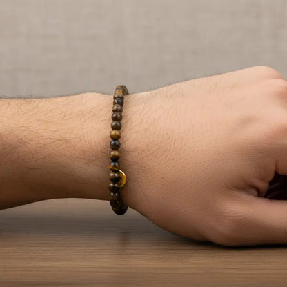Tiger Eye Beaded Bracelet with gold charm on a wrist rest upon wood with grey background