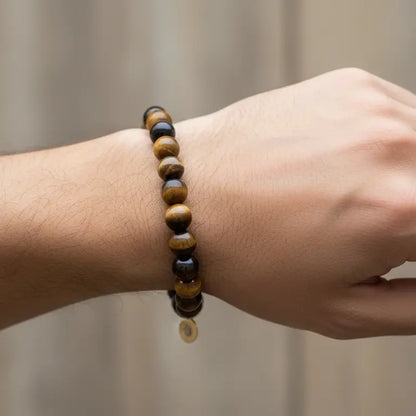 Tiger Eye Beaded Bracelet with gold charm on a wrist and blurred neutral background