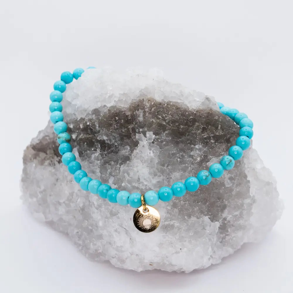 Turquoise Beaded Bracelet with gold charm on a white and black stone and light background