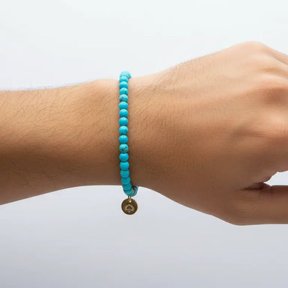 Turquoise Beaded Bracelet with gold charm on a wrist and neutral background