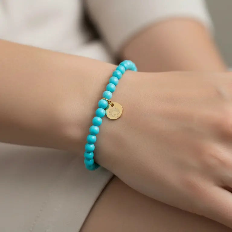 Turquoise Beaded Bracelet with gold charm on a wrist with blurred background