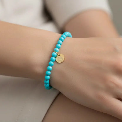 Turquoise Beaded Bracelet with gold charm on a wrist with blurred background