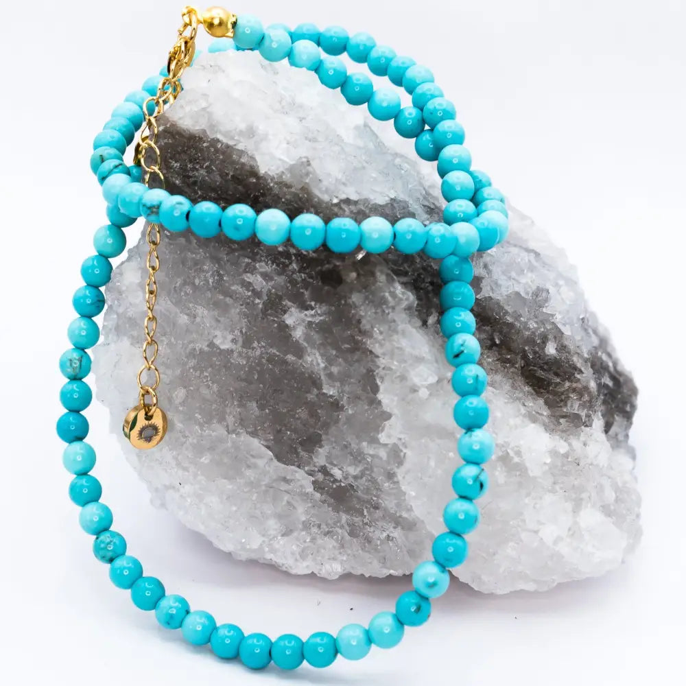 Turquoise Beaded Necklace with gold charm on a grey and white stone with light grey background 