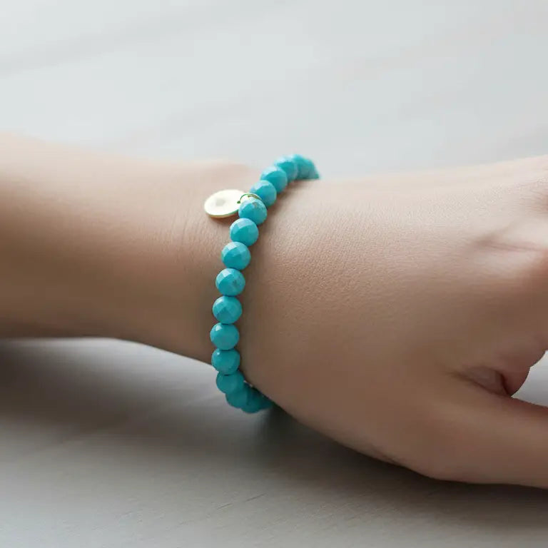 Turquoise Faceted Bracelet with gold charm on a wrist and light grey background