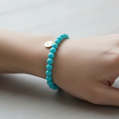 Turquoise Faceted Bracelet with gold charm on a wrist and light grey background
