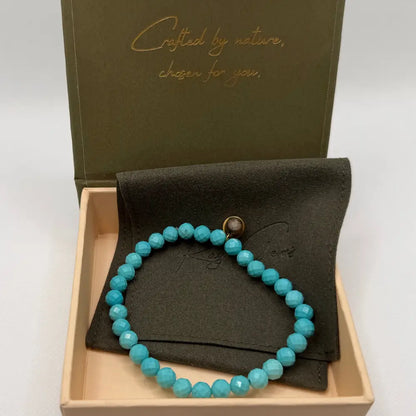 Turquoise Faceted Bracelet with gold charm on an olive green pouch in cream and olive green branded box and neutral background